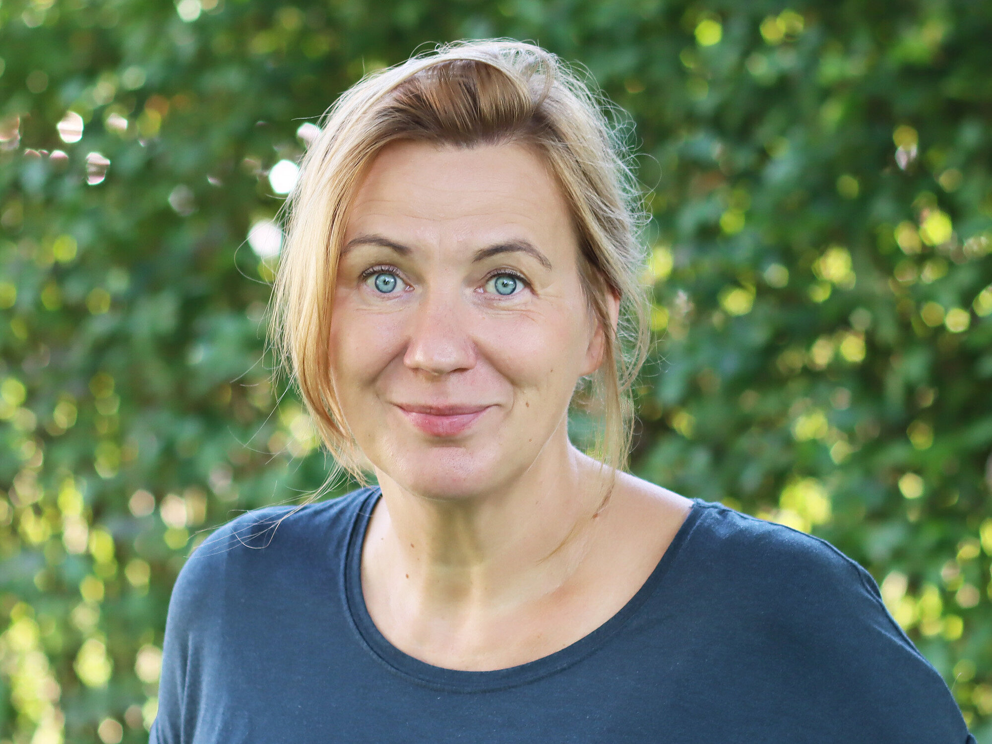 Manja Olbrich Porträt einer Frau mit hellen Augen und blondem, zurückgebundendem Haar.