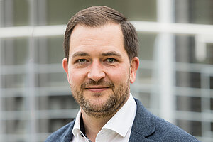 Ein Mann mit dunkelbraunen kurzen Haaren und Bart schaut in die Kamera.