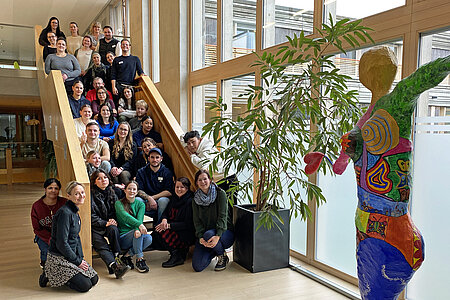 Rund 30 Personen, die alle in Richtung Kamera schauen, stehen und sitzen auf einer Freitreppe im Inneren eines Klinikgebäudes.