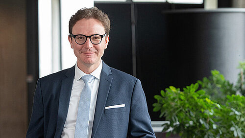 Ein freundlich aussehender Mann im mittleren Alter mit Brille im blauen Anzug