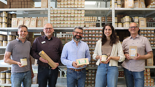 Bio-Gewürze aus Kißlegg: Kooperation mit SoulSpice Vor einem großen, hohem Regal mit lauter Gewürzpackungen stehen fünf Personen nebeneinander. Sie alle halten eine Gewürzpackung in den Händen und schauen freundlich in die Kamera.